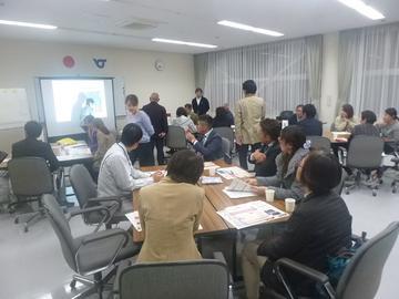 スクリーンの横で話をしている人の話を聞いている参加者達の写真