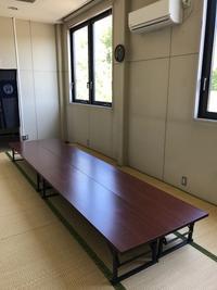 エヤコンの下に長机が並べられた和室の部屋の写真