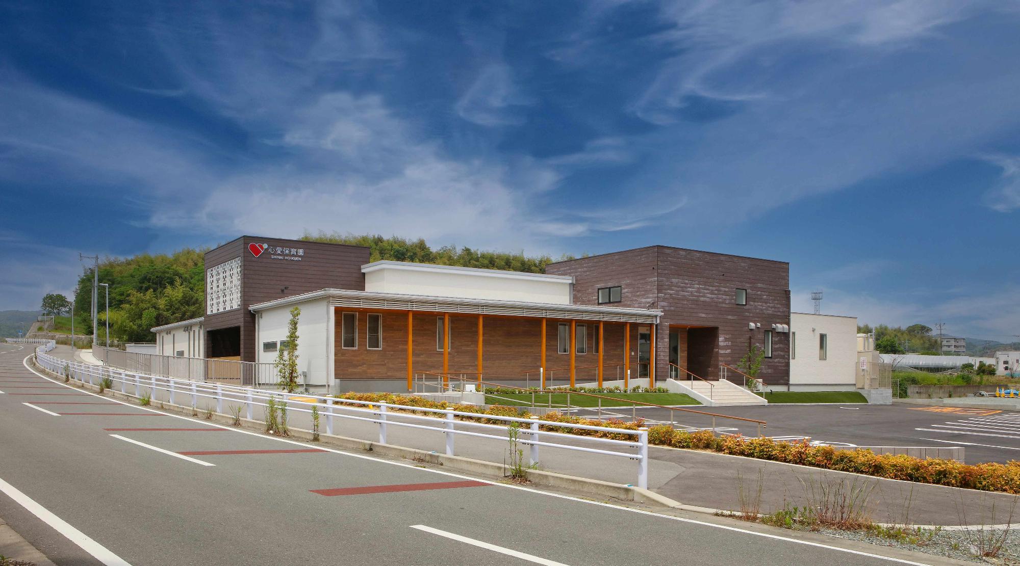 心愛ほいくえんと書かれたボードがフェンスに張ってあり2階建ての建物や遊具が写っている写真