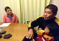 子どもを膝に乗せて食卓に座っているお父さんと、その様子を見ているお母さんの写真