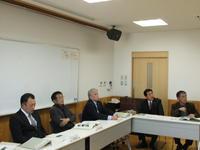 設置された机に5名の男性が座り会議に参加している写真