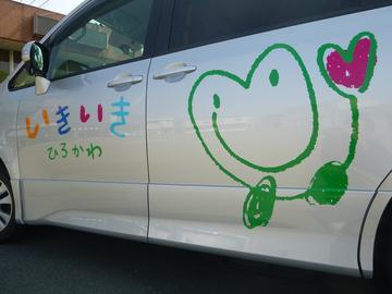 「いきいきひろかわ」の文字とハートのシンボルマークが描かれているシルバー色の車を左側から写した写真
