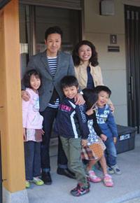 玄関の前で笑顔の鹿毛さん家族6人の写真