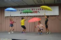 ウェルカムパーティーで水色、緑、ピンク、黄色の傘をさしパフォーマンスをしている写真