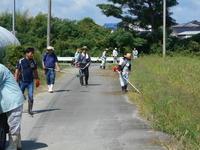 草刈り機を使い道路横を環境美化活動している参加者の人達の写真