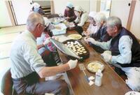 公民館内で長机を囲み料理を食べている高齢者の方々の写真