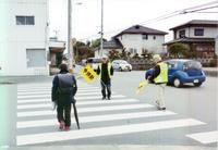 老人クラブ2名の方が横断歩道を渡る児童を黄色の旗を持ち安全に渡れるように見守っている写真